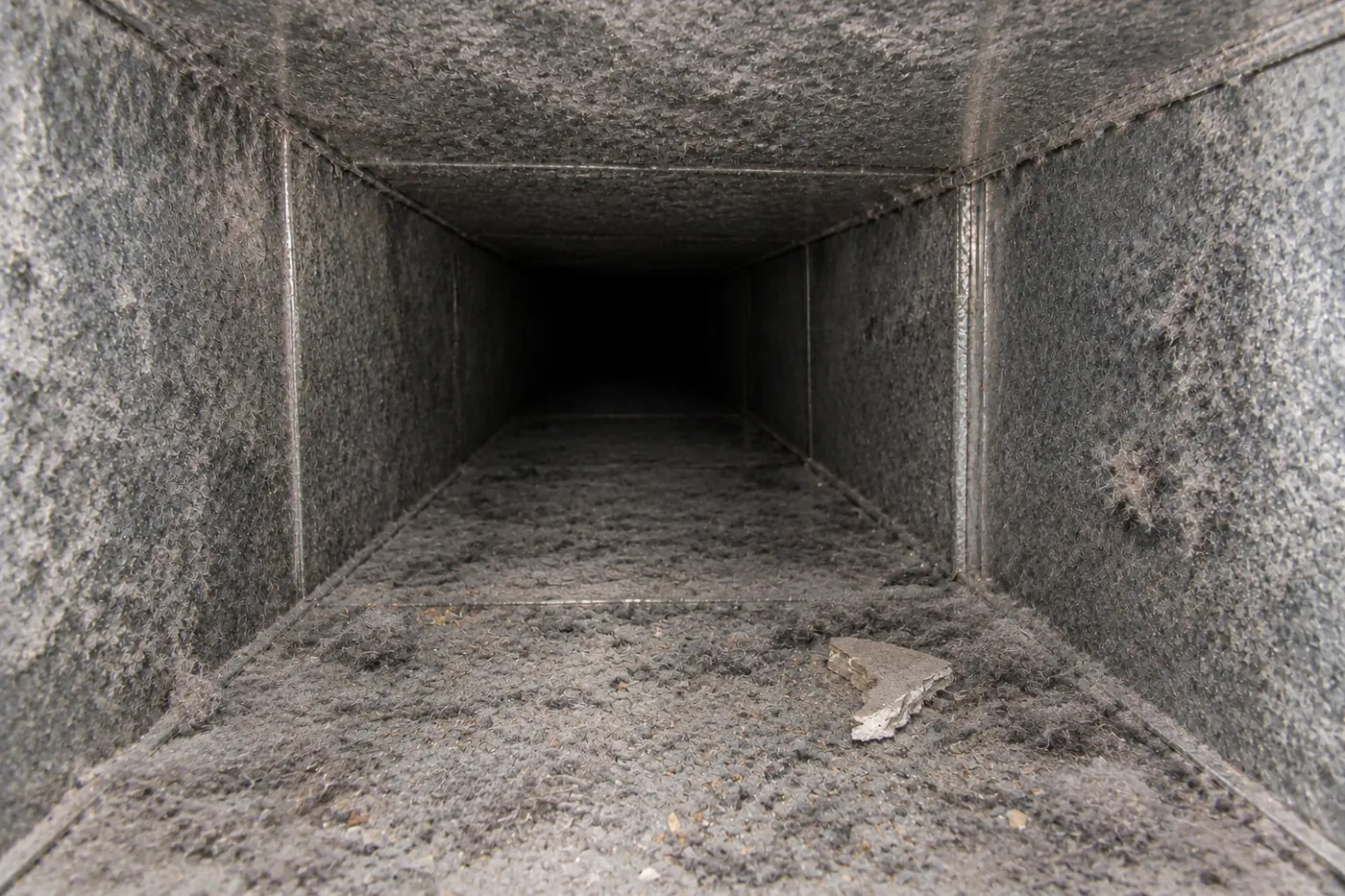 An air duct before cleaning, coated in dust, lint and debris
